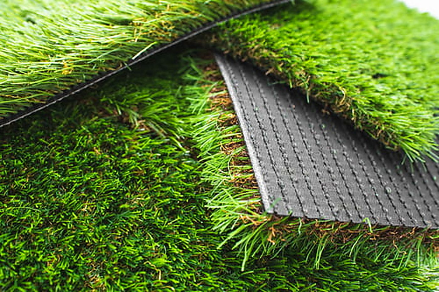 Close-up of artificial turf backing and seam edge showing where repair work is needed