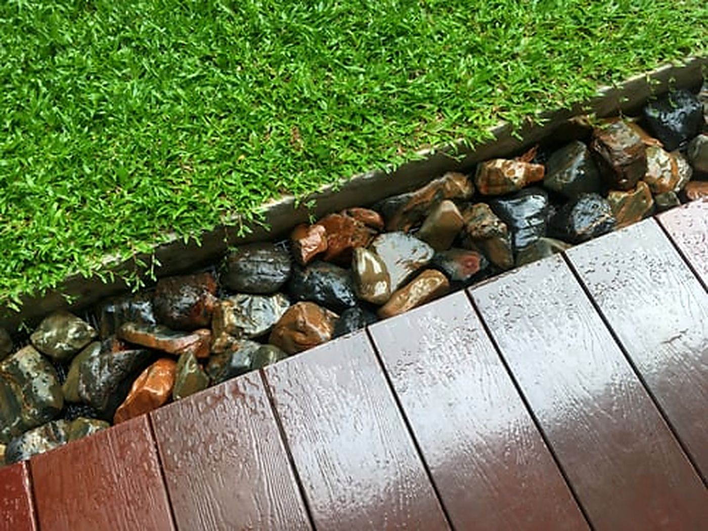 Artificial turf edge and seam detail bordered by river rock and wood decking after professional repair